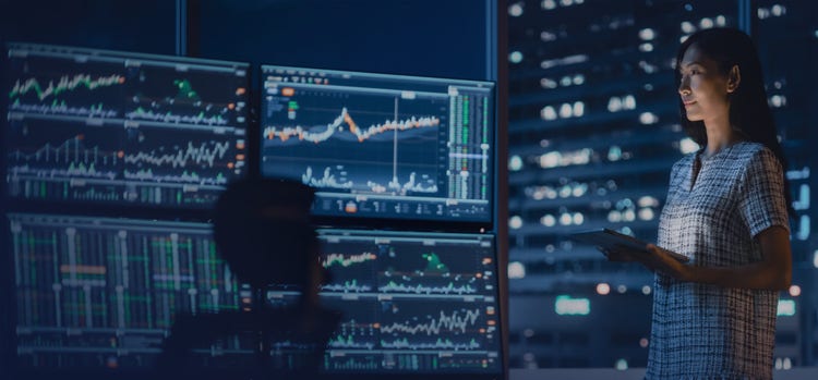 A woman looking at multiple screens showing data and graphs