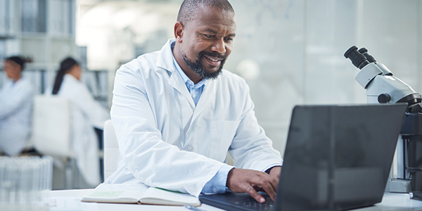 A smiling man sitting at a desk and working on a laptop