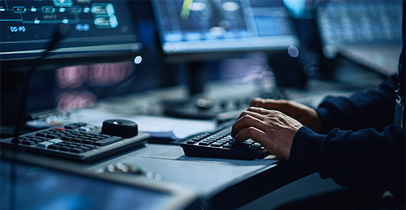 Close up view of a pair of hands on a keyboard in front of monitors.