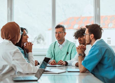 A group of medical professionals sitting around a table, in a meeting