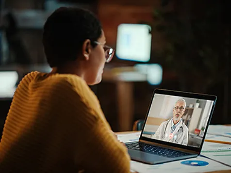 Woman sitting at a table, having a video call with a doctor on a laptop