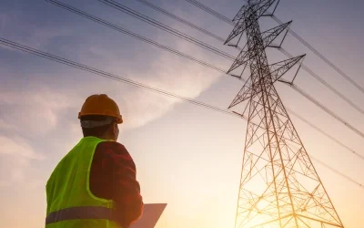 A lineman looking up at an electricity grid structure
